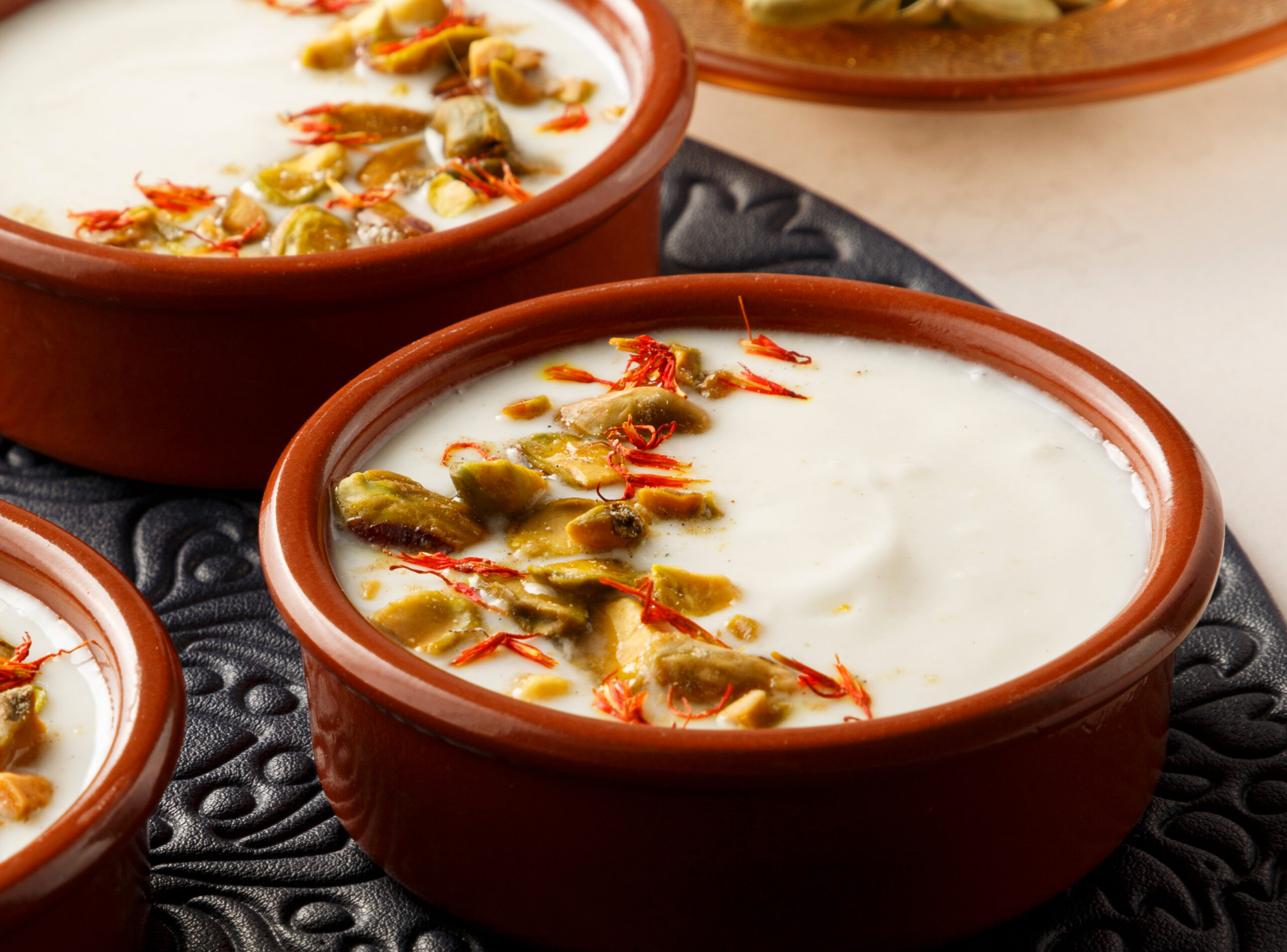 Image of a brown bowl with a rich yogourt dessert in it and garnished with dry fruits and saffron. Image of a brown bowl with a rich yogourt dessert in it and garnished with dry fruits and saffron.